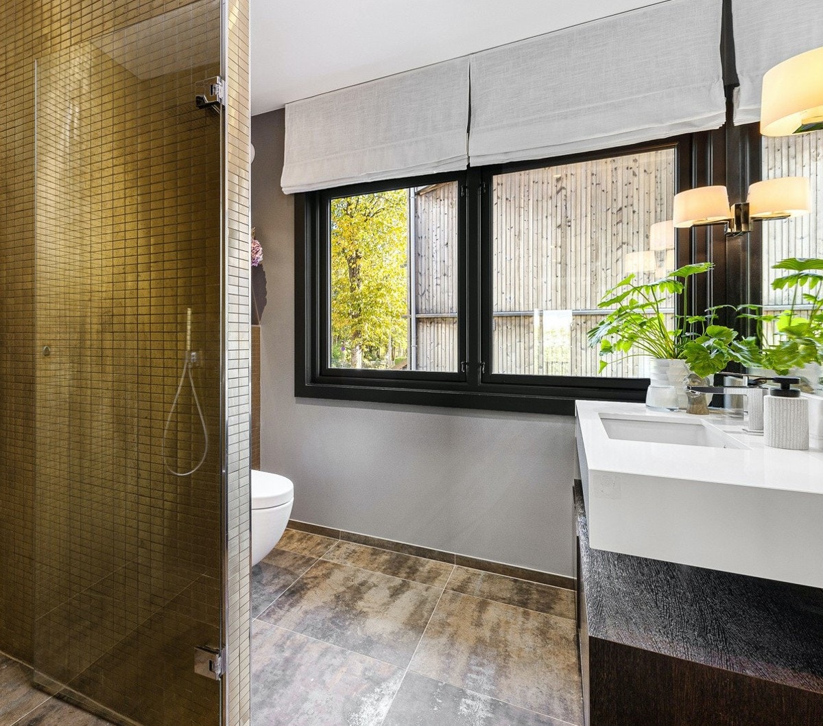 Stilrent bad med gulvvarme, romslig dusjhjørne med gullfargede fliser, baderomsinnredning snekret av møbelsnekker med "svevende", heldekkende servant og vegghengt toalett. Galleribilde