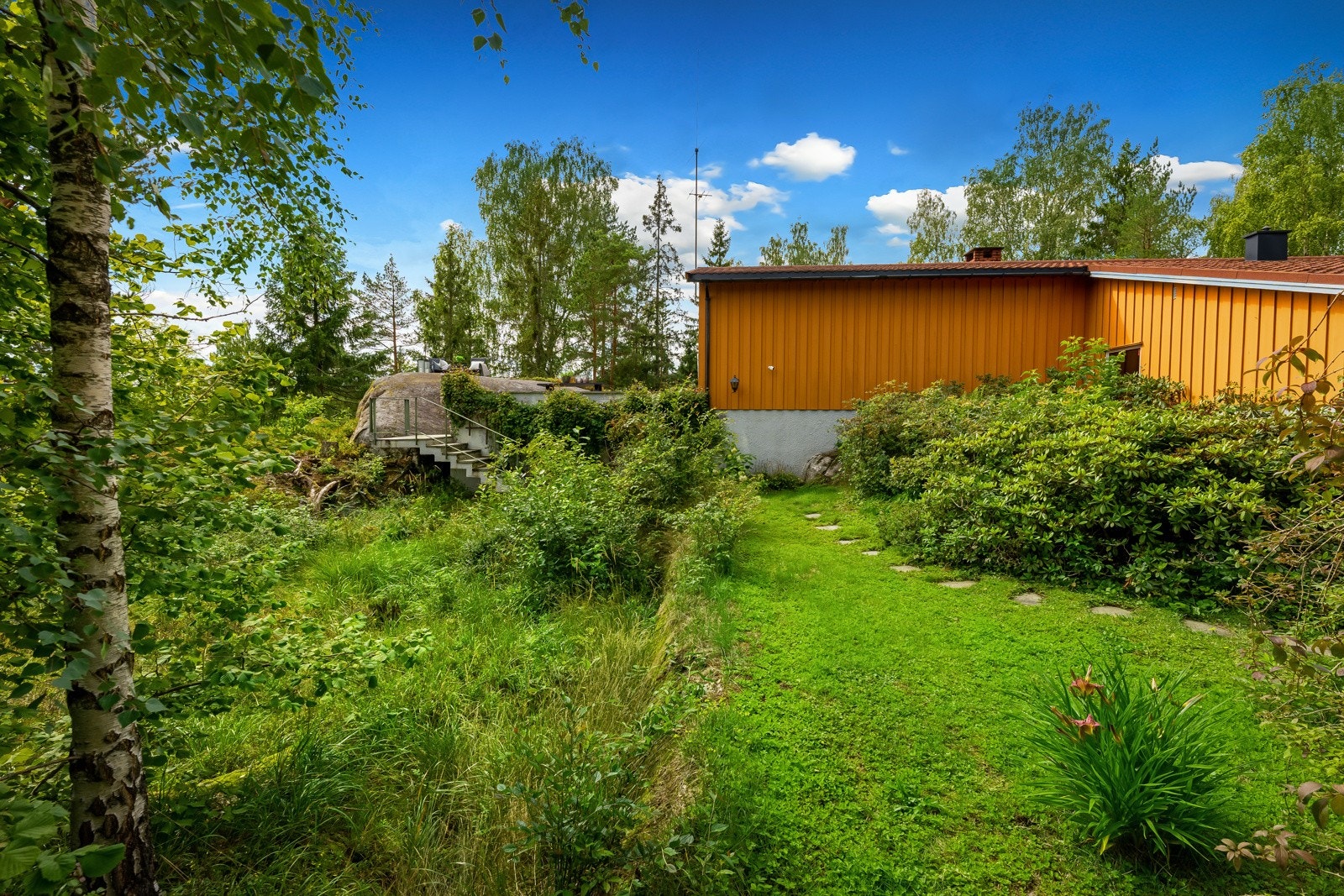 Frodig, pent beplantet tomt der boligen likker godt tilpasset terrenget Galleribilde
