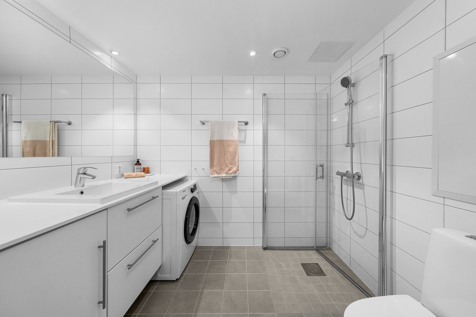 Leiligheten har et pent bad med flislagte gulv- og veggoverflater. Badet har vannbåren gulvvarme, og det er opplegg for vaskemaskin under benkeplaten. Galleribilde