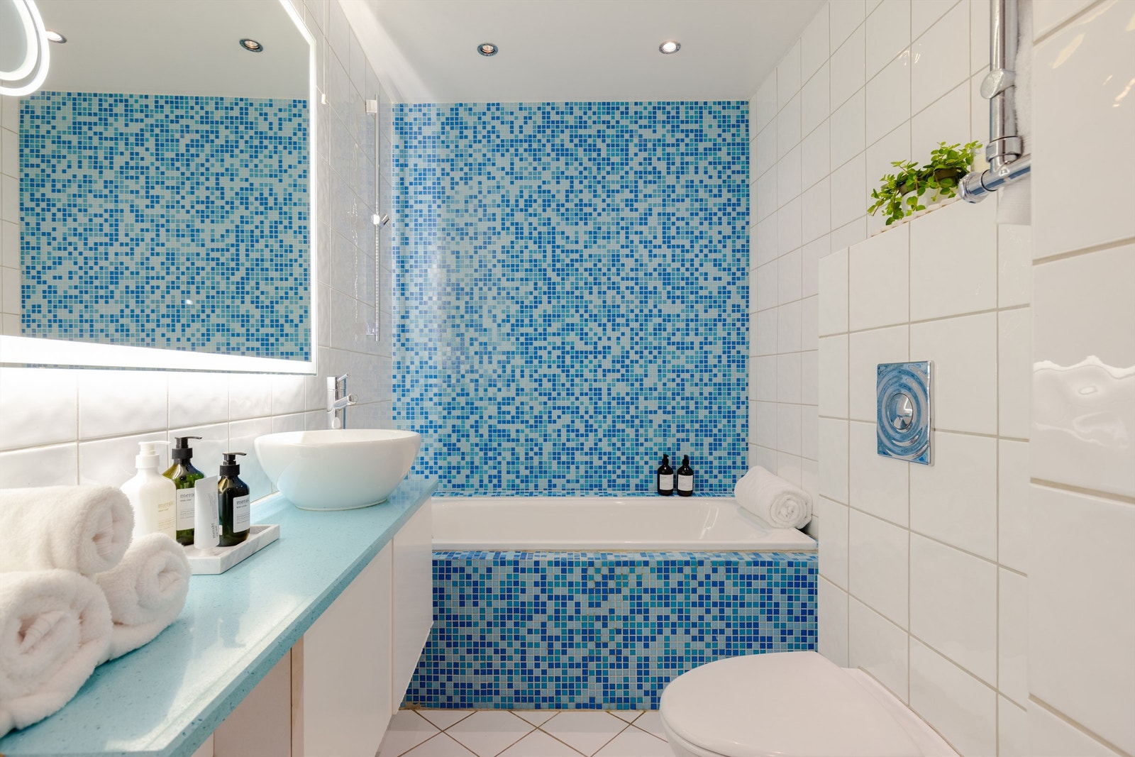 Badet har servant på vegghengt skapinnredning, stort speil med belysning, samt innmuret badekar. Galleribilde