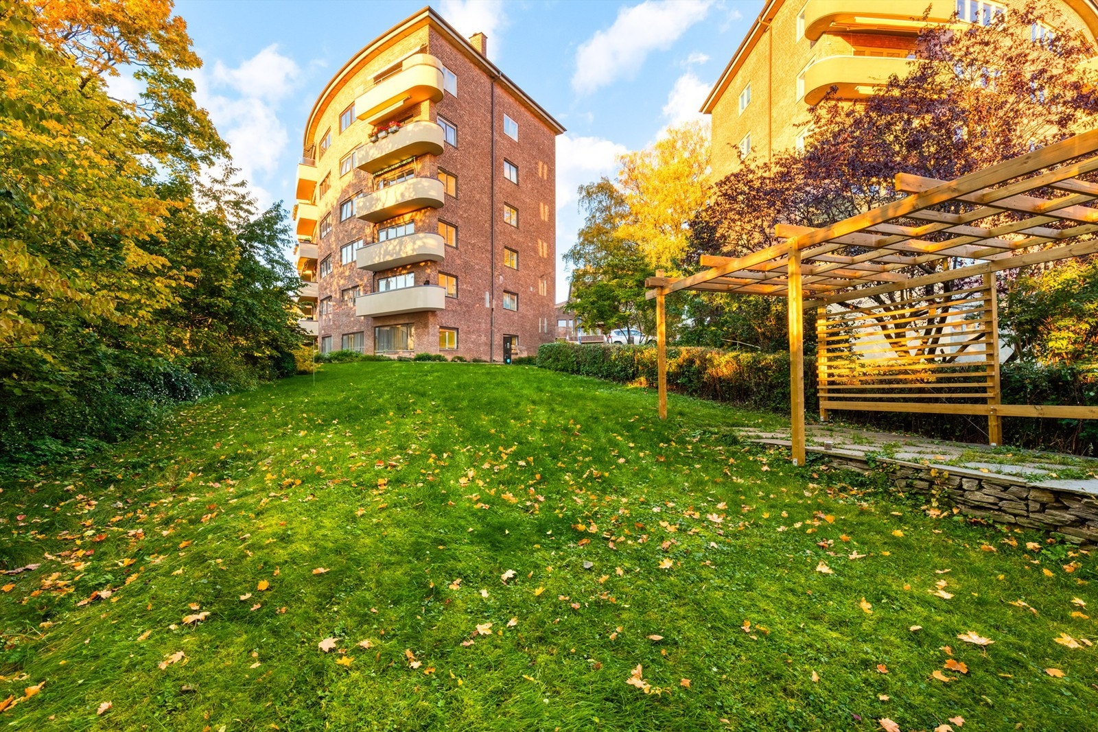 Parkmessig opparbeidet felleshage med stor gressplen, prydbusker, pergola og sittegrupper. Galleribilde