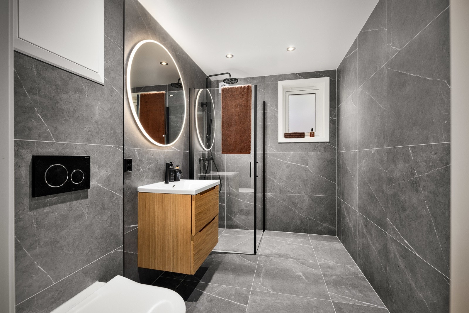 Bad nr 2. i underetasjen ble pusset opp i 2023 og har fått moderne farger og stil. Badet har grå marmor lignende fliser på vegger og gulv. I gulvet er det elektriske varmekabler. Badet har veggenhengt toalett, servant, speil med belysning og dusjhjørne. Galleribilde