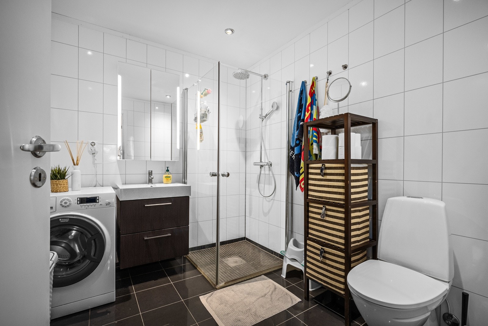 Badet har baderomsplater på veggene og flislagte gulv. I gulvet er det elektriske varmekabler. I himlingen er det downlights. Badet har gulvstående toalett, servant, speil med belysning, dusjhjørne og opplegg for vaskemaskin. Galleribilde