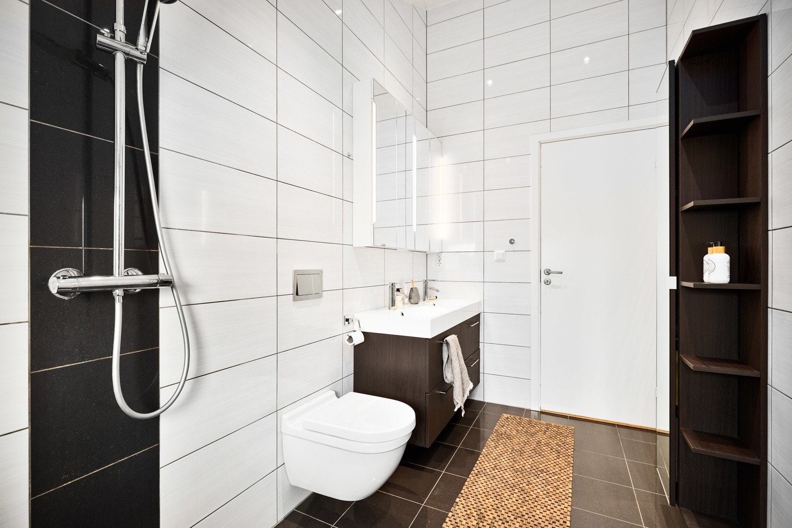 Badet har vegghengt toalett, servant med speilskap over og dusjhjørne. I taket er det downlights og det er belysning i speilet. Galleribilde