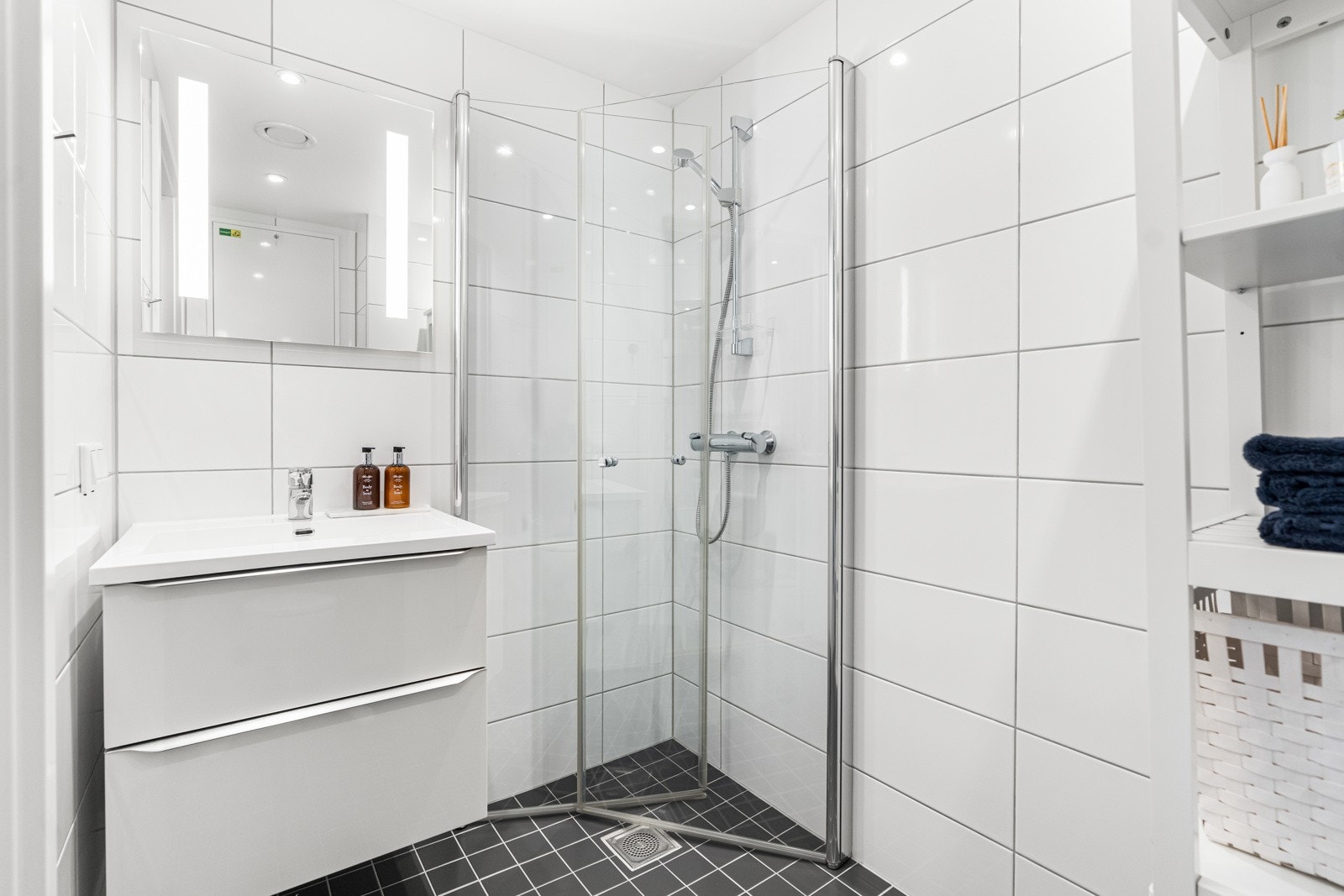 Badet i 1. etasje. Innredningen består av et underskap, servant, speil med lys, stikk og en dusjsone med dusjing direkte på gulv og vegg. Galleribilde