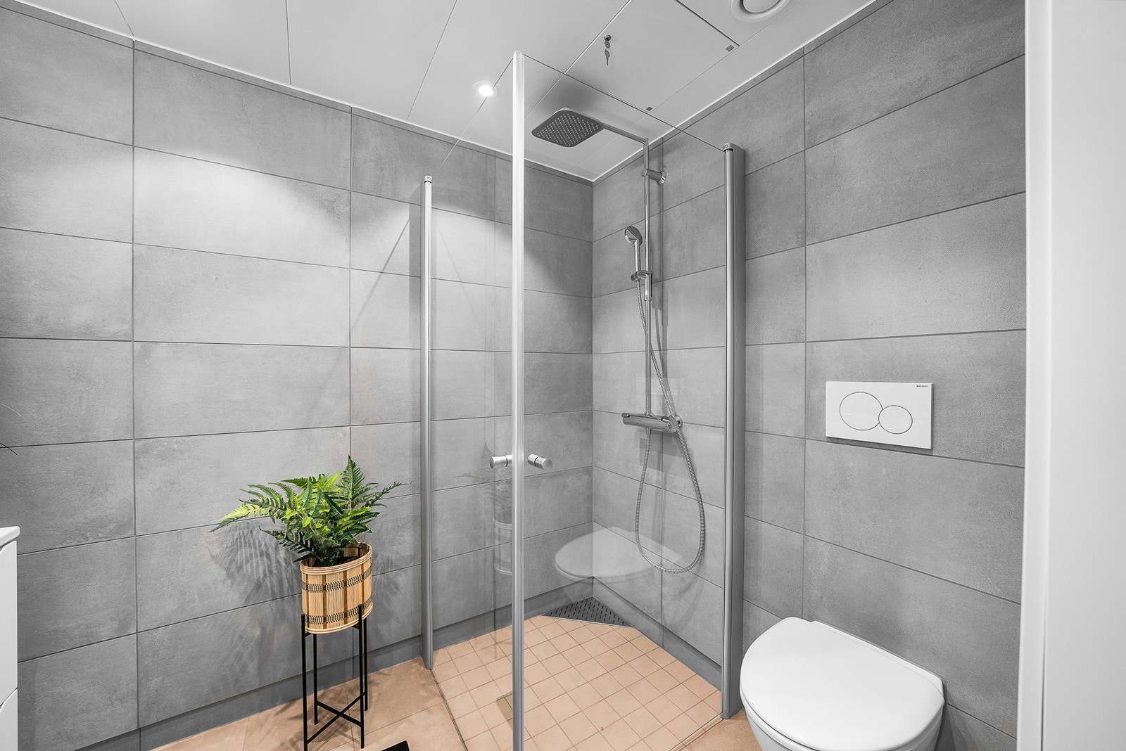 Badet er utstyrt med regndusj i et dusjhjørne med innfellbare glassvegger, vegghengt wc og servantinnredning med underskap. Galleribilde