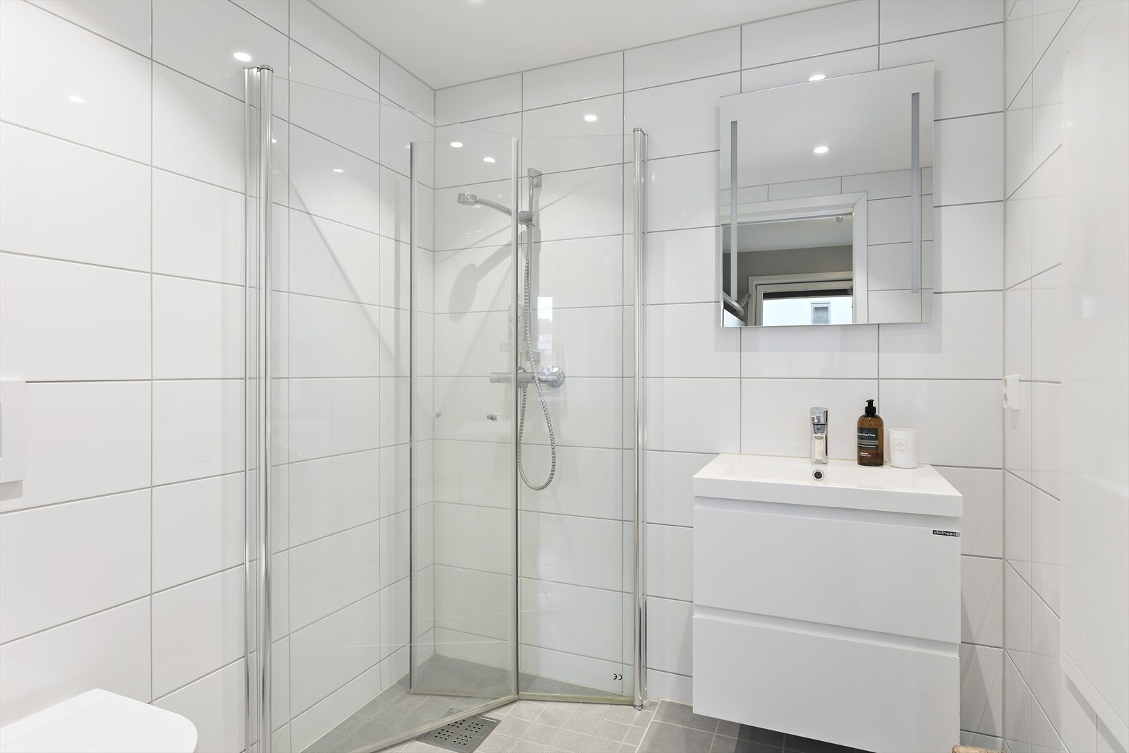 Badet har innredning med nedfelt servant, veggmontert toalett, dusjvegger/hjørne og opplegg for vaskemaskin. Galleribilde