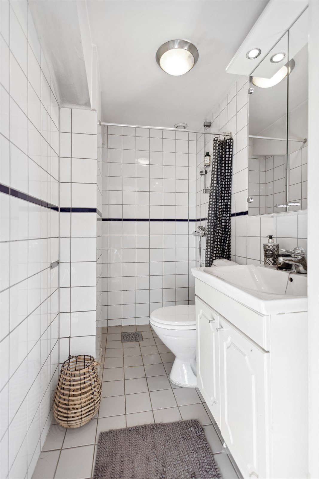 Badet har tidløse, hvite veggfliser og grå fliser på gulv med gulvvarme. Galleribilde