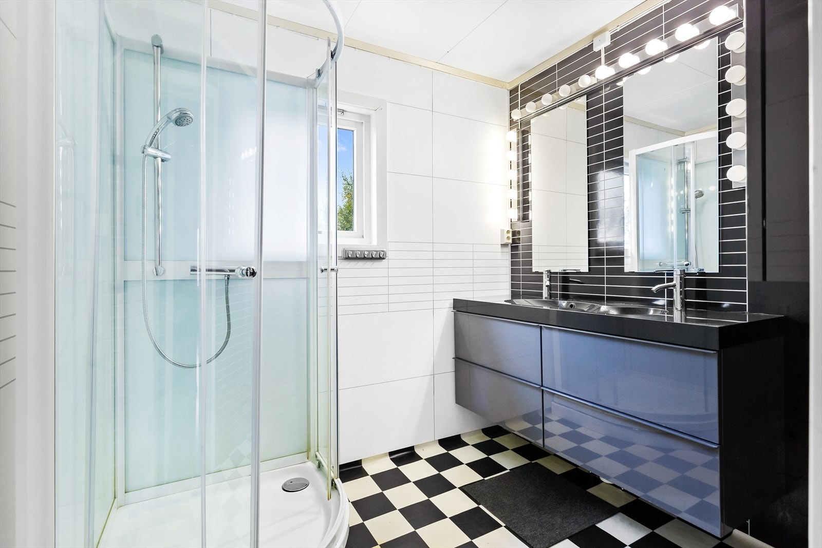 Badet i andre etasje ble pusset opp i 2013 og fremstår som lekkert med sjakkbrettmønstret belegg på gulv, hvite flisplater på vegg og belysning rundt speil. Her er det helstøpt, sort dobbelservant på servantmøbel med grå høyglansfronter og dusjkabinett. Galleribilde