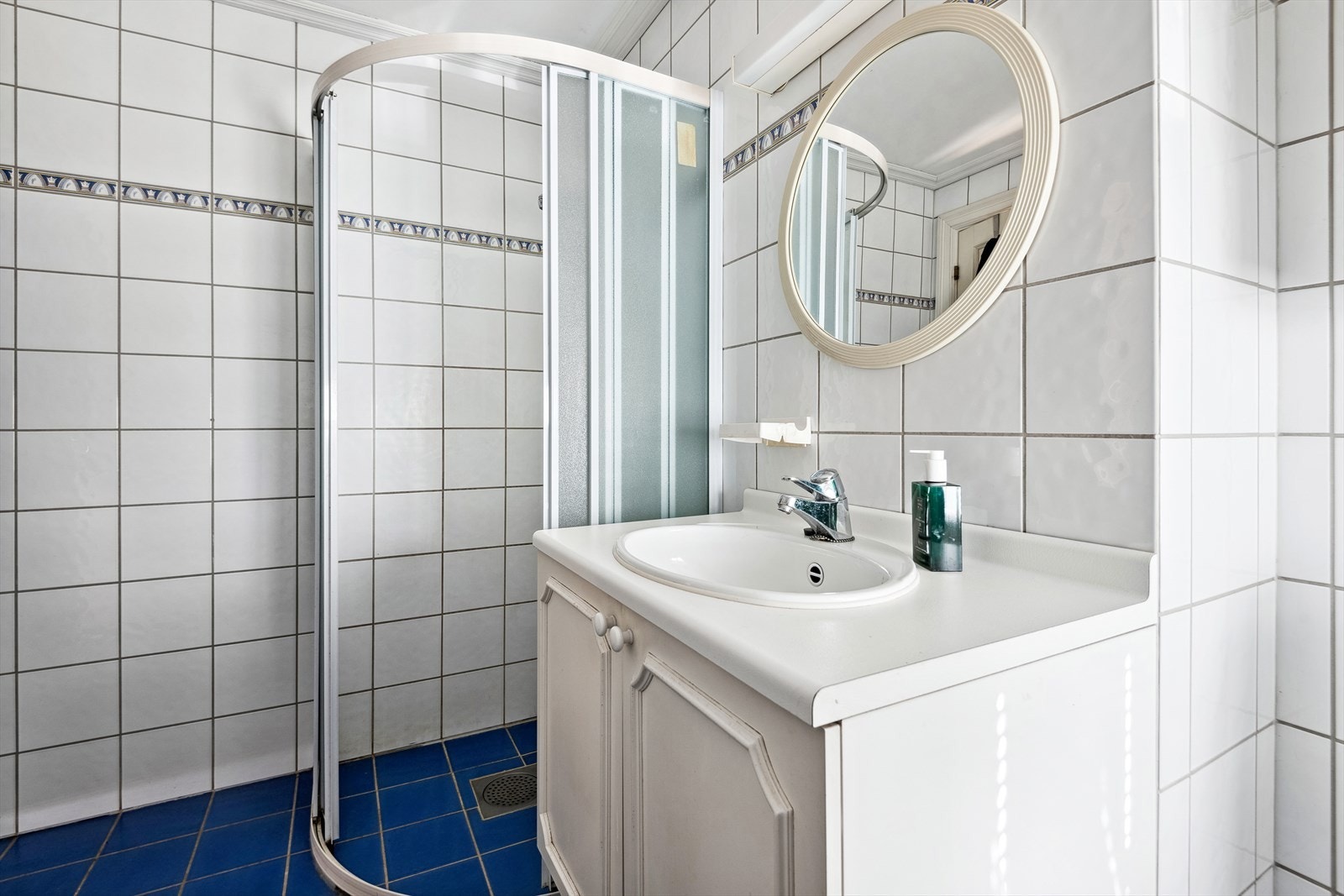 Badet er bestående av gulvstående toalett, servant, speil og dusjhjørne. Galleribilde