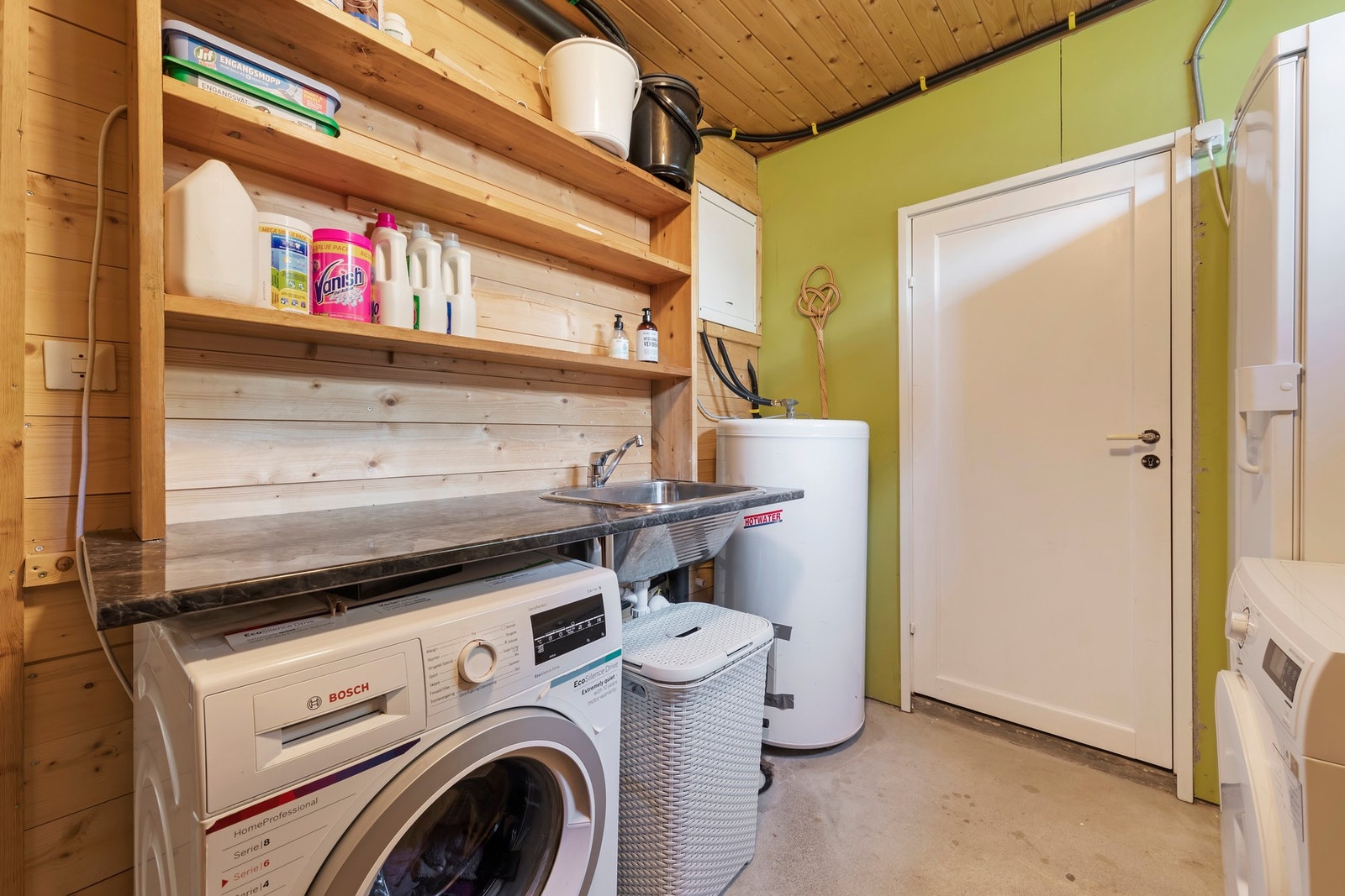 Vaskerom har ubehandlet betonggulv, malte murvegger og panel på vegger og i innvendig tak. Opplegg for vaskemaskin og skyllekar nedfelt i benkeplate Galleribilde