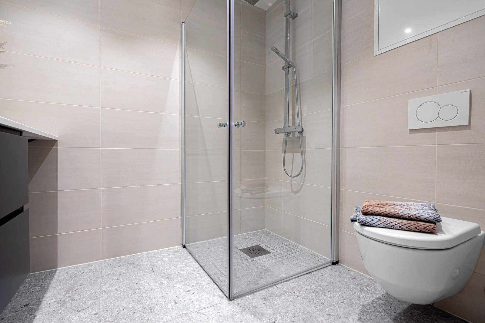 Badet har pene fliser på gulv og vegger. Det er dusj med svingbare dører, og oppgradert dusjgarnityr og dusjarmatur fra Tapwell. Veggmontert toalett fra Laufen. Galleribilde