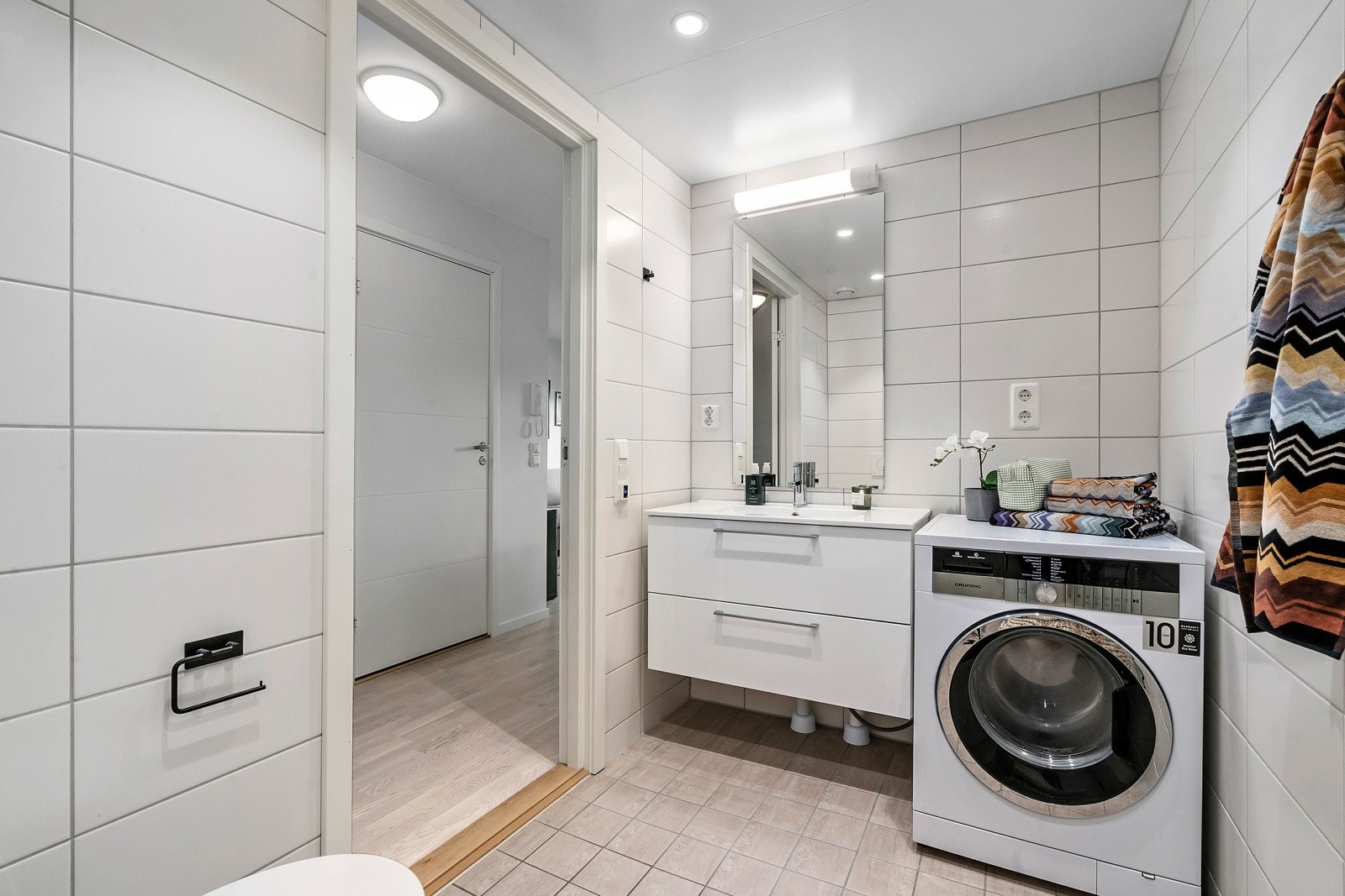 Flislagt bad med opplegg til vaskemaskin. Lys over speil og toalettet er vegghengt. Galleribilde