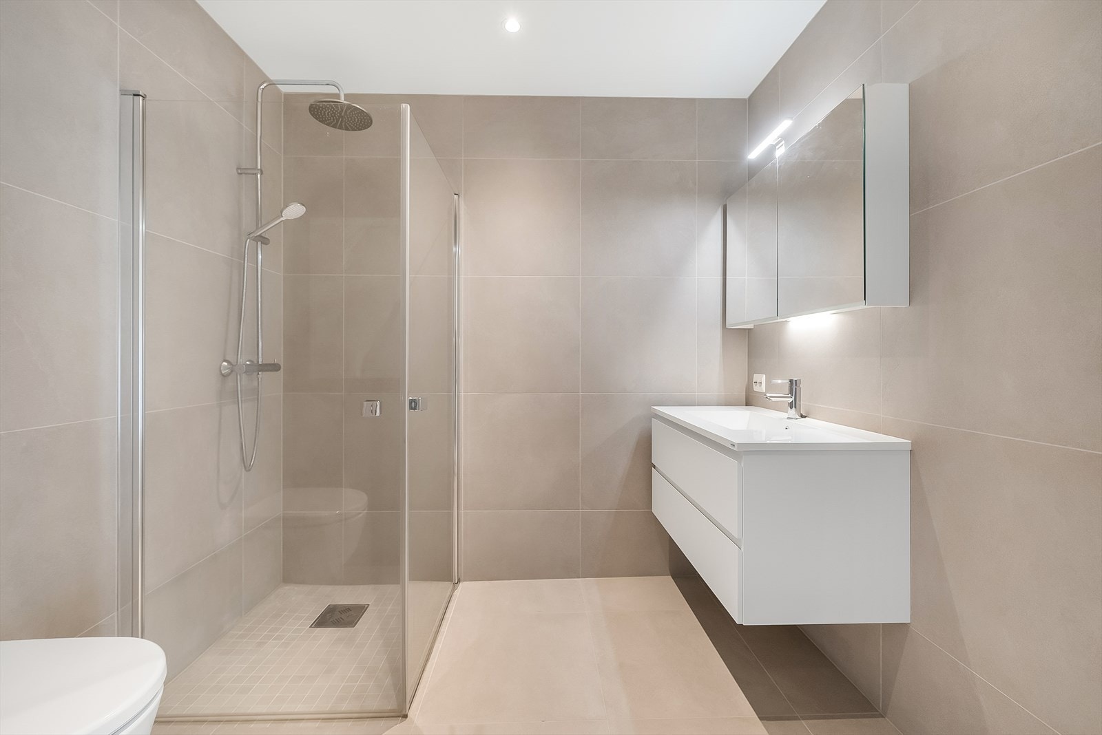 Delikat innredet bad med fliser på gulv og vegger. Badet er pent innredet med baderomsinnredning, toalett og dusjnisje. Galleribilde