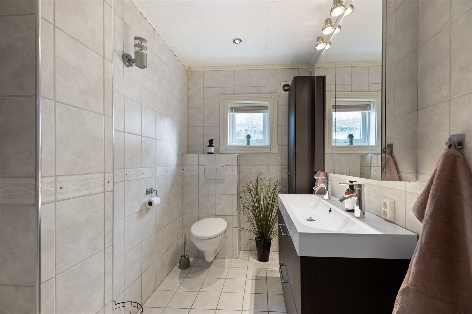 Rommet er innredet med heldekkende servant over innredning med skuffer. Vegghengt skap, speil, belysning og vegghengt toalett. Galleribilde