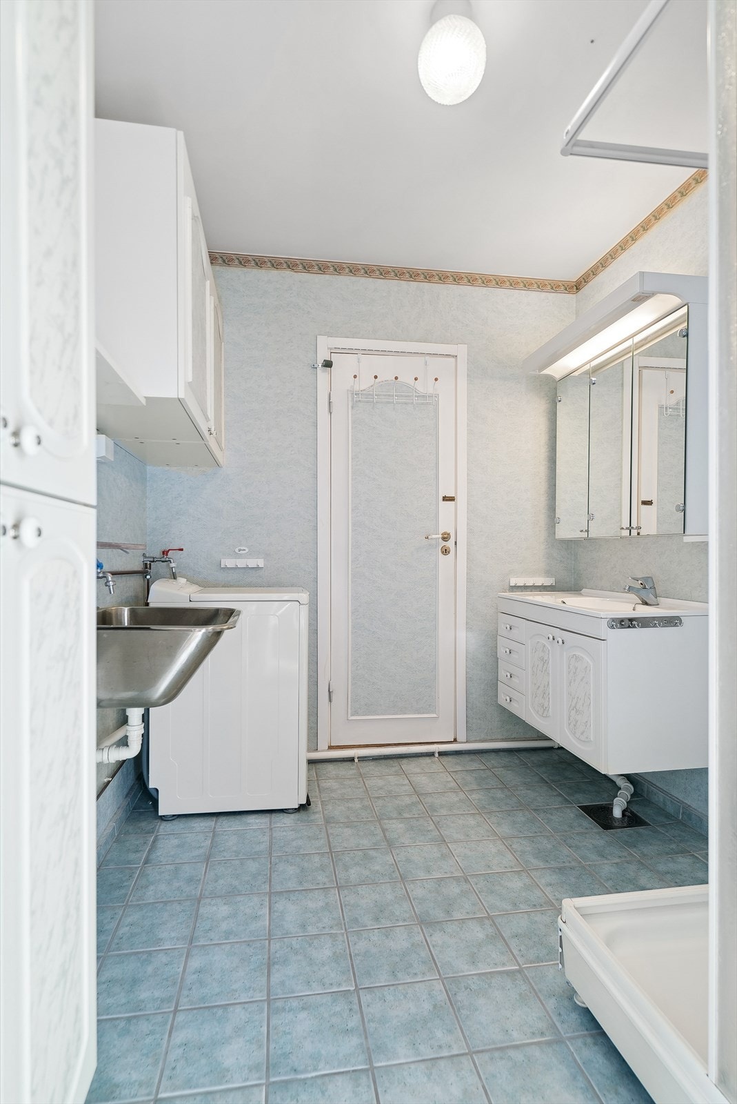 Bad med flislagt gulv, opplegg for vaskemaskin og utslagsvask på vegg. Galleribilde