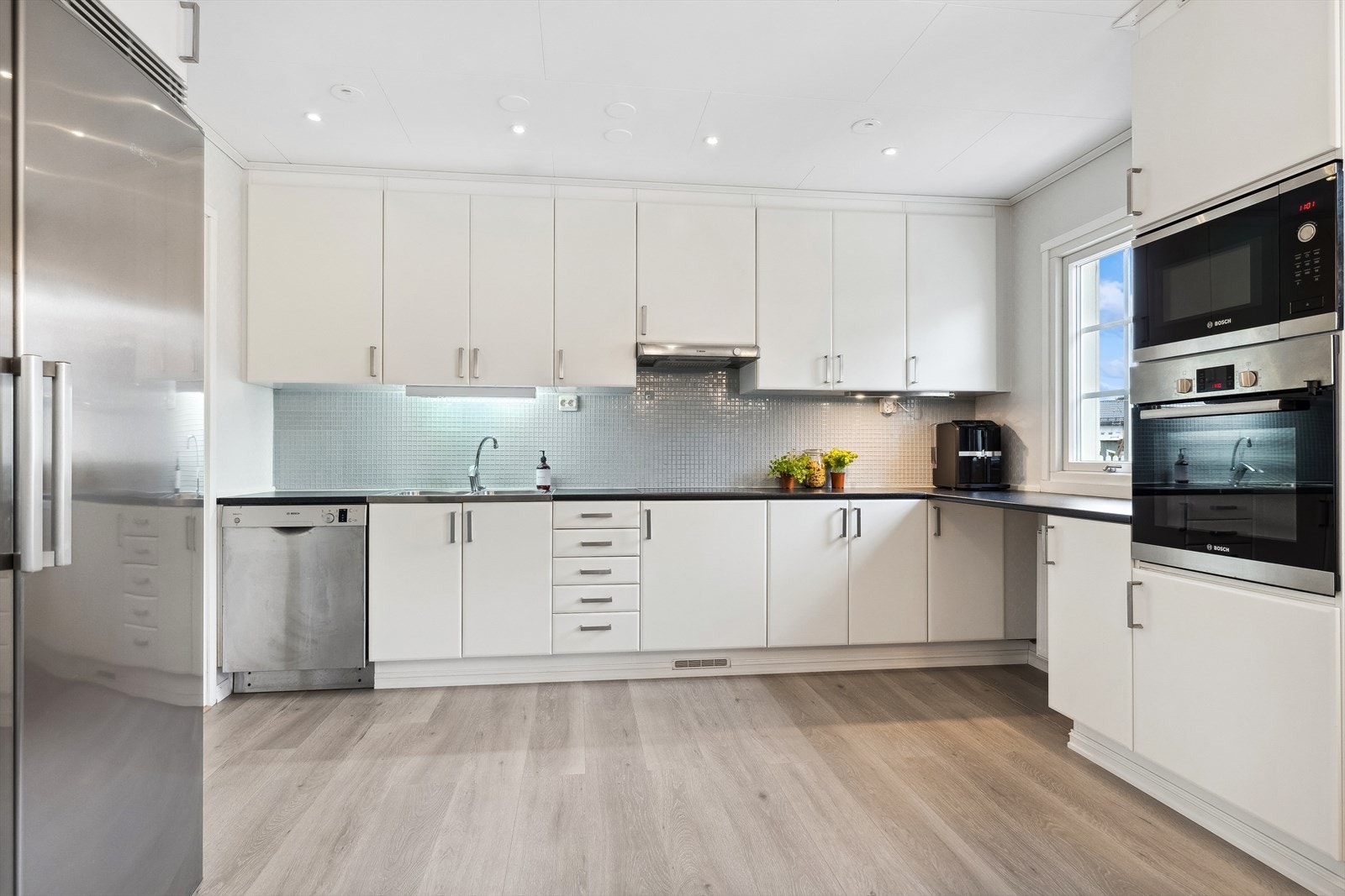 Funksjonelt og lyst kjøkken i moderne utførelse. Det er kjøkkeninnredning med malte, slette fronter og laminert benkeplate. Galleribilde