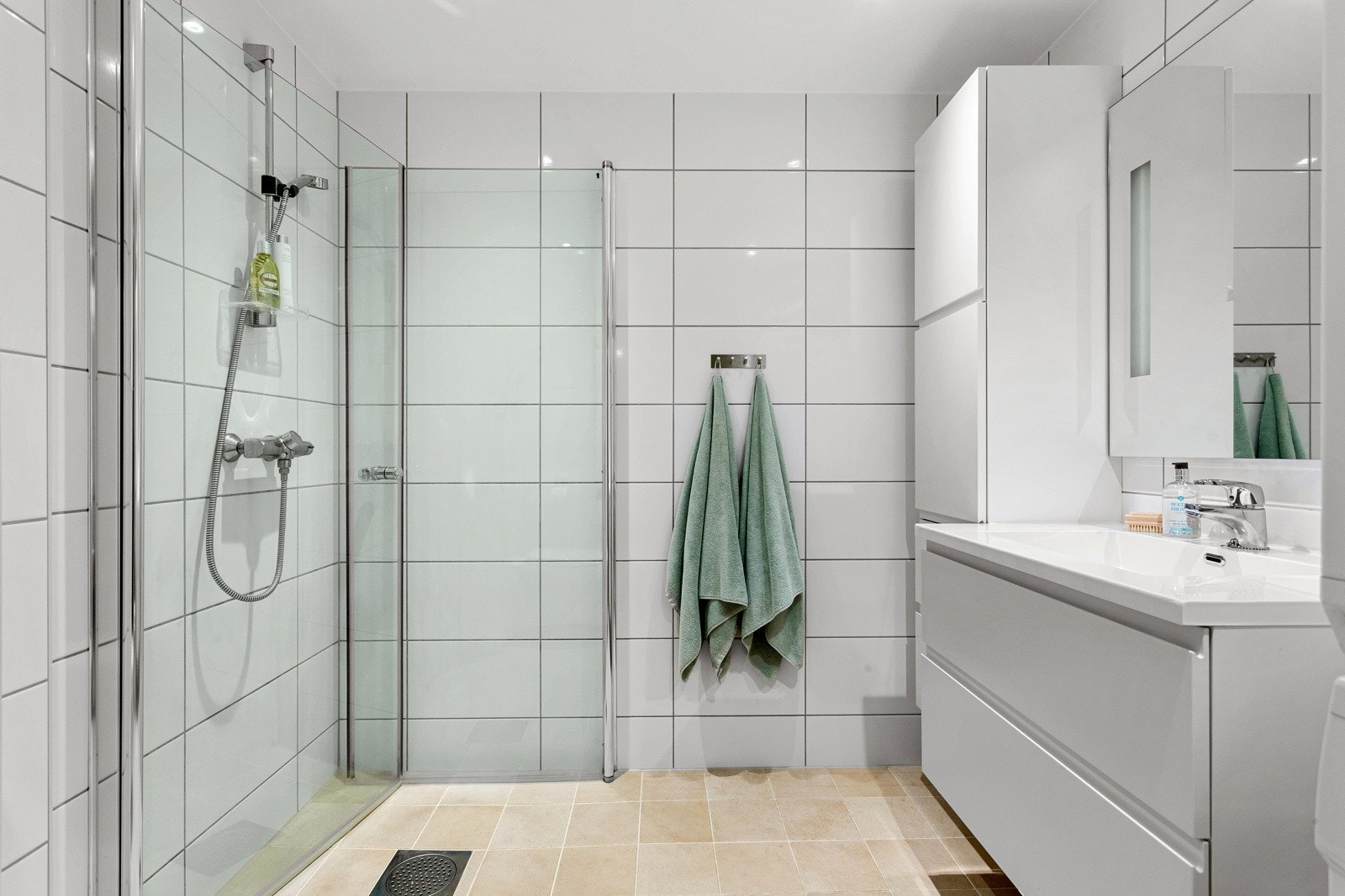 Moderne baderomsinnredning med skuffer og heldekkende servant, speil med integrert belysning over og vegghengt høyskap ved siden av. Galleribilde