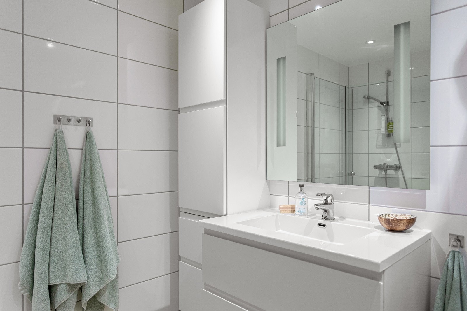 Moderne baderomsinnredning med skuffer og heldekkende servant, speil med integrert belysning over. Galleribilde