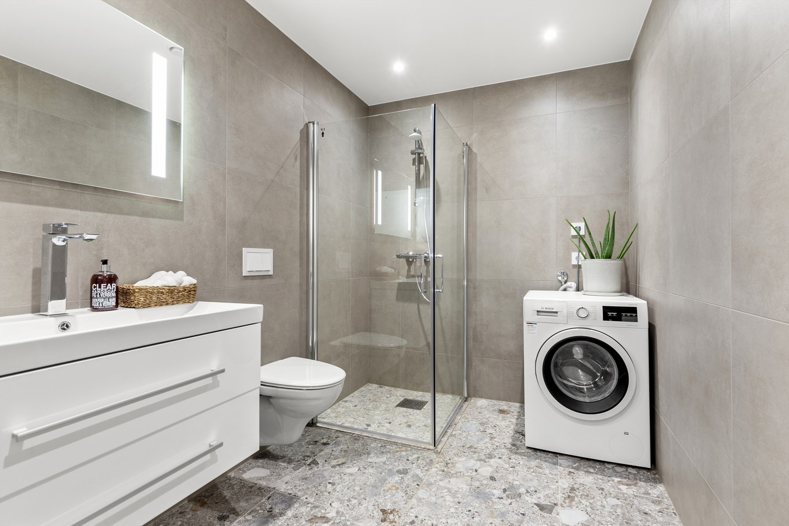 Badet i 1. etasje har innredning med nedfelt servant, veggmontert toalett, dusjvegger/hjørne og opplegg for vaskemaskin Galleribilde