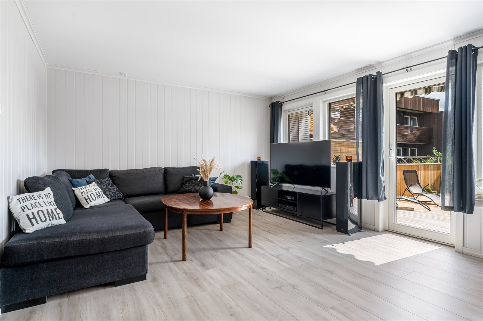 Pen laminat på gulv og lyse panelplater på vegger. Den ene stueveggen er malt opp i en behagelig, blå kontrastfarge som gir fin dybde til rommet. Galleribilde
