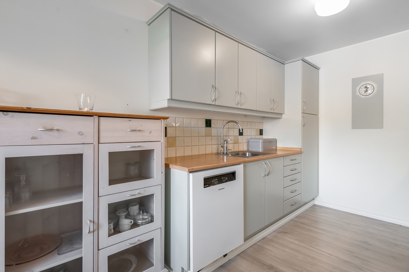 Keramiske flis på vegg over laminat benkeplate med gode arbeidsflater, nedfelt platetopp og nedfelt oppvaskkum i rustfritt stål. Galleribilde