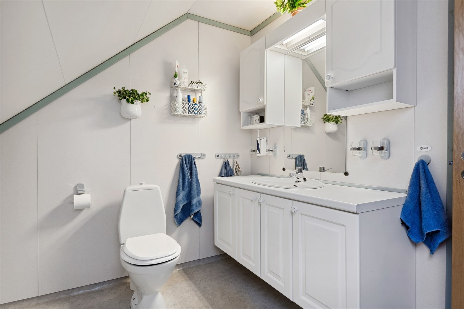 Badet har en hvit laminat benkeplate, samt underskap og overskap med hvite profilerte fronter. Galleribilde