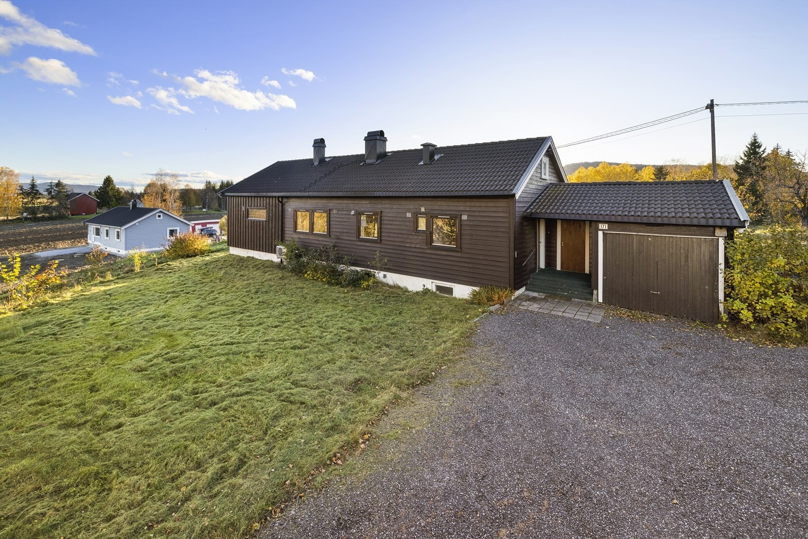 Pent opparbeidet uteområde med gruset innkjøring/gårdsplass, plen og diverse beplantning. Galleribilde