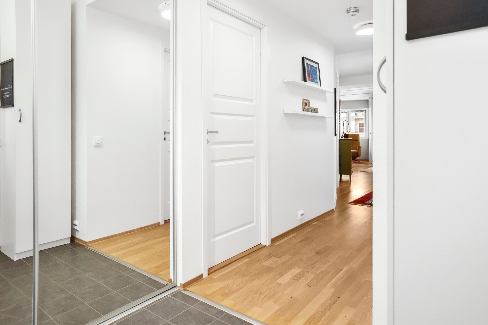 Romslig entré med flislagt gulv og skyvedørsgarderobe med speildører Galleribilde