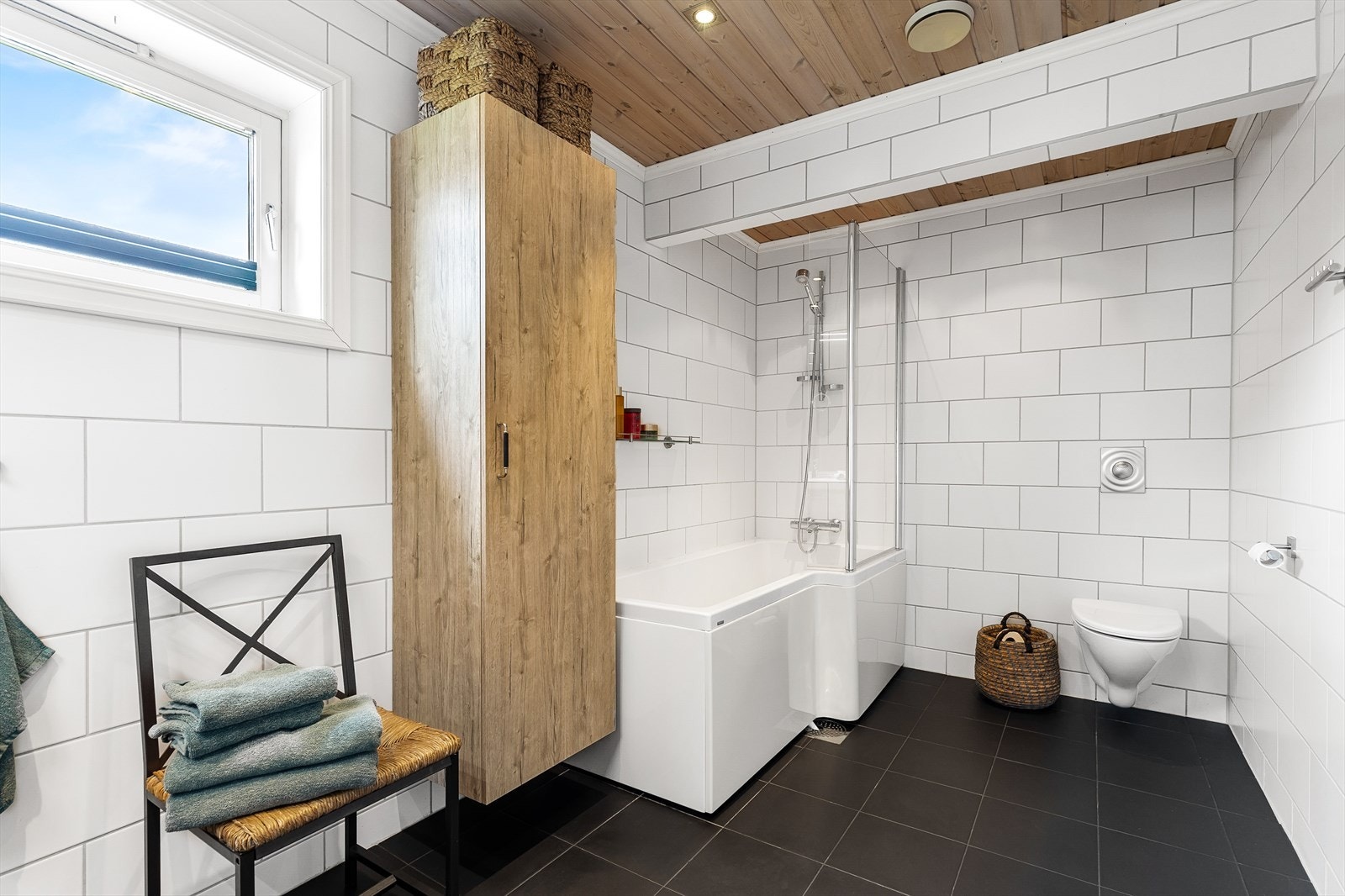 Innredning på badet består av vegghengt wc, badekar med dusjvegg av glass, samt doble servanter i skuffeseksjon med sideskap, høyskap, speil og belysning Galleribilde