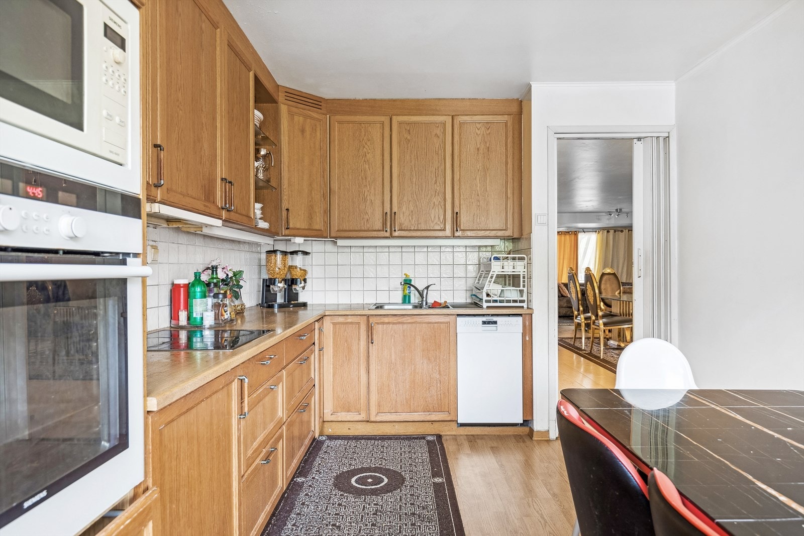 Kjøkkeninnredning med profilerte trefargede fronter, benkeplater i laminat, rustfri oppvaskkum med avrenningsplate, ventilator, opplegg for oppvaskmaskin og integrerte hvitevarer. Galleribilde