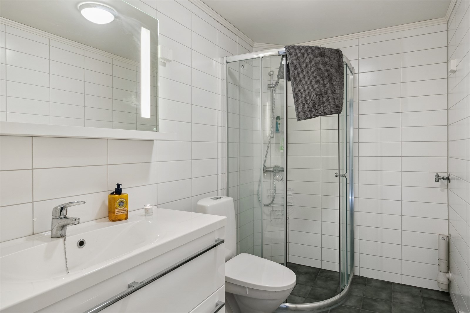 Badet er innredet med baderomsinnredning med servant, gulvmontert toalett og dusjhjørne, samt opplegg for vaskemaskin/tørketrommel. Flislagte vegger og gulv med varmekabler. Galleribilde