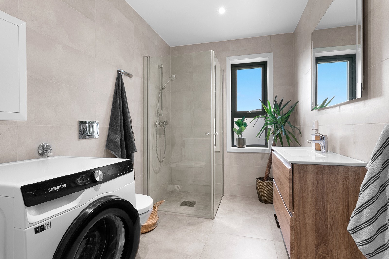 Delikat flislagt bad med vegghengt toalett, servant med innredning, dusjhjørne og opplegg for vaskemaskin Galleribilde