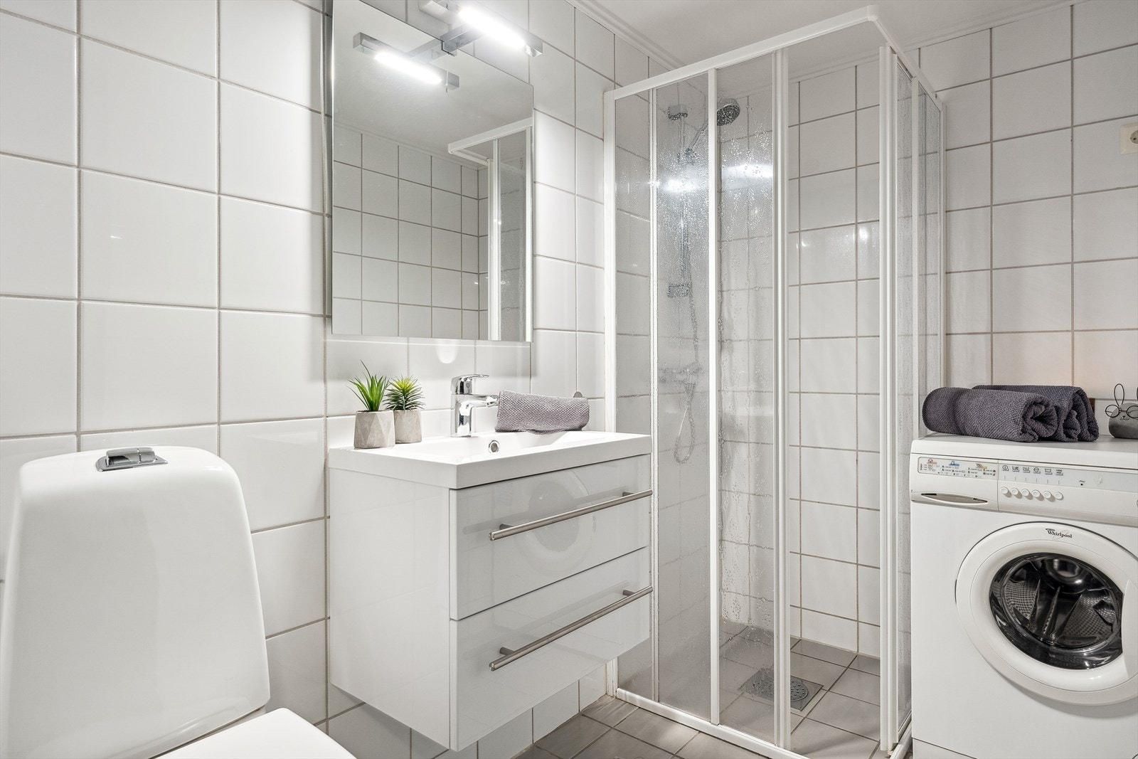Bad 1 med flislagte overflater og varmekabler i gulv, innredning med nedfelt servant, toalett, dusjvegger og opplegg for vaskemaskin. Galleribilde