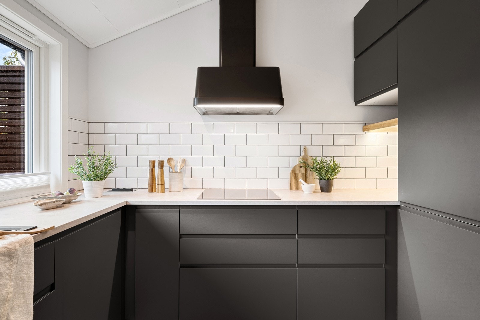 Over deler av benken er det belysning og hvite metrofliser, og over kokesonen er det installert en stilig ventilator i sort utførelse. Galleribilde