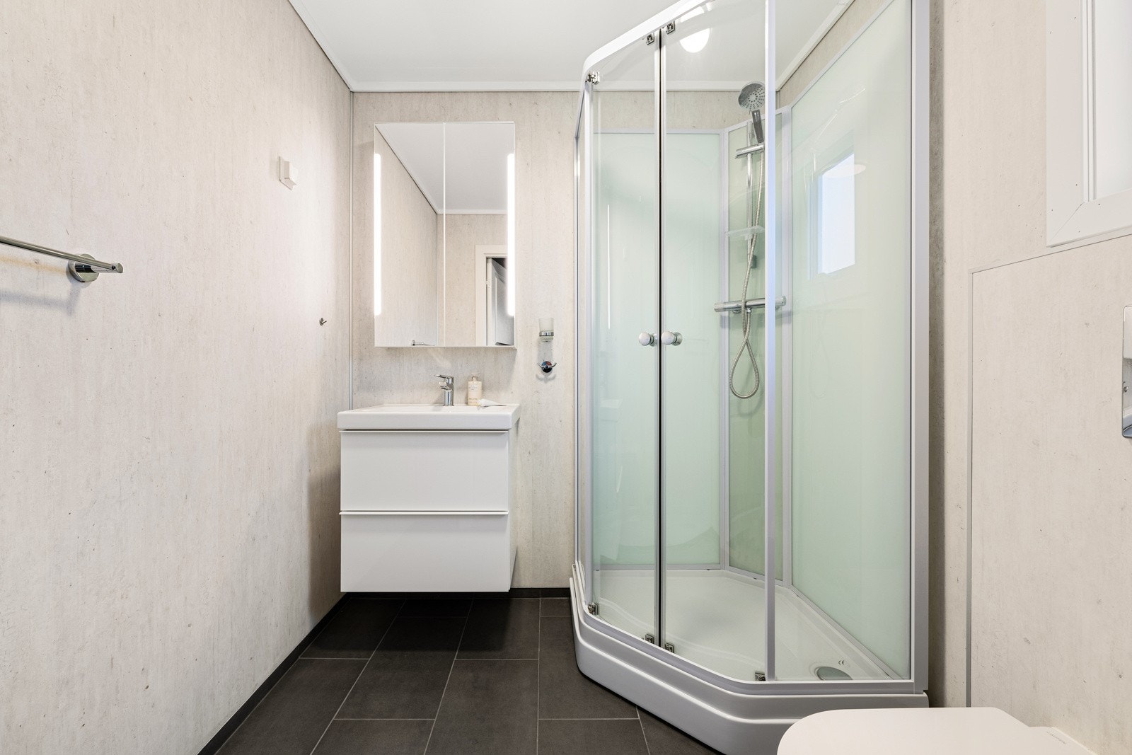 Badet ble pusset opp i 2022 med sorte gulvfliser og grå våtromsplater på veggene. Galleribilde