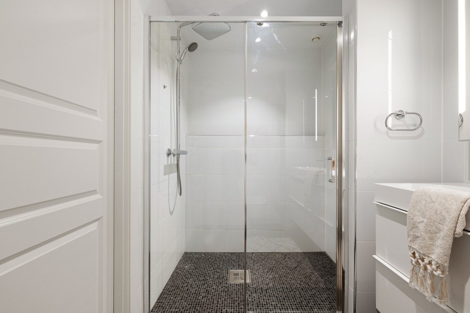 En romslig dusjnisje er utstyrt med skyvedører, mosaikkfliser og stor regnfallsdusj. Galleribilde