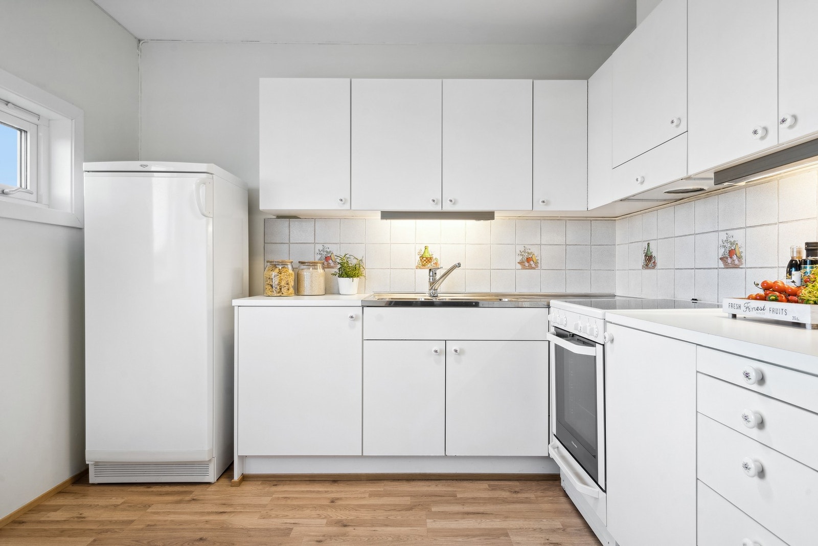 Innredning med hvite slette fronter, benkeplate av laminat og fliser på vegg over benk. Frittstående hvitevarer. Galleribilde