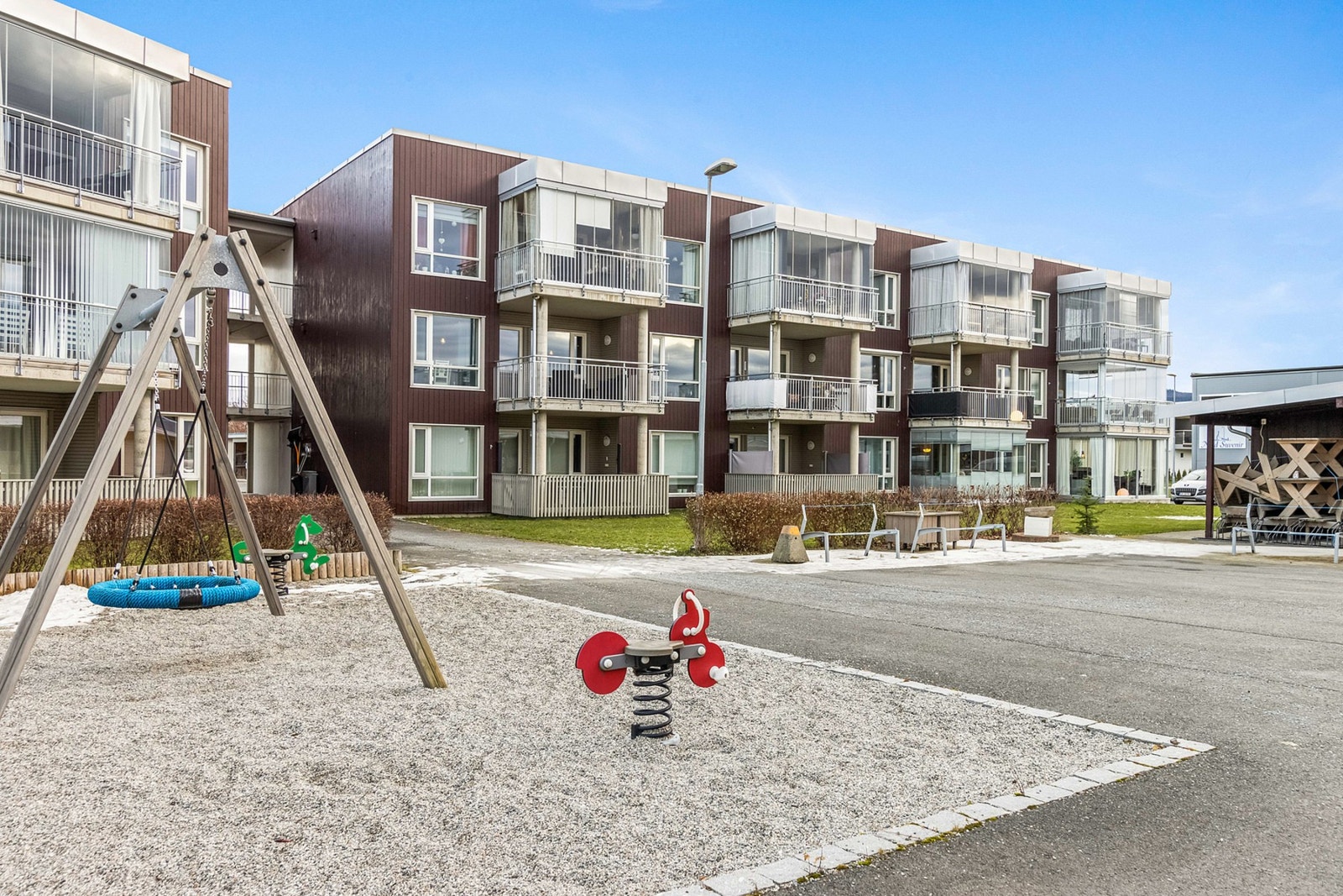 Pent opparbeidet fellesareal med lekeplass, plen, beplantninger, belegningsstein og asfalt. Galleribilde