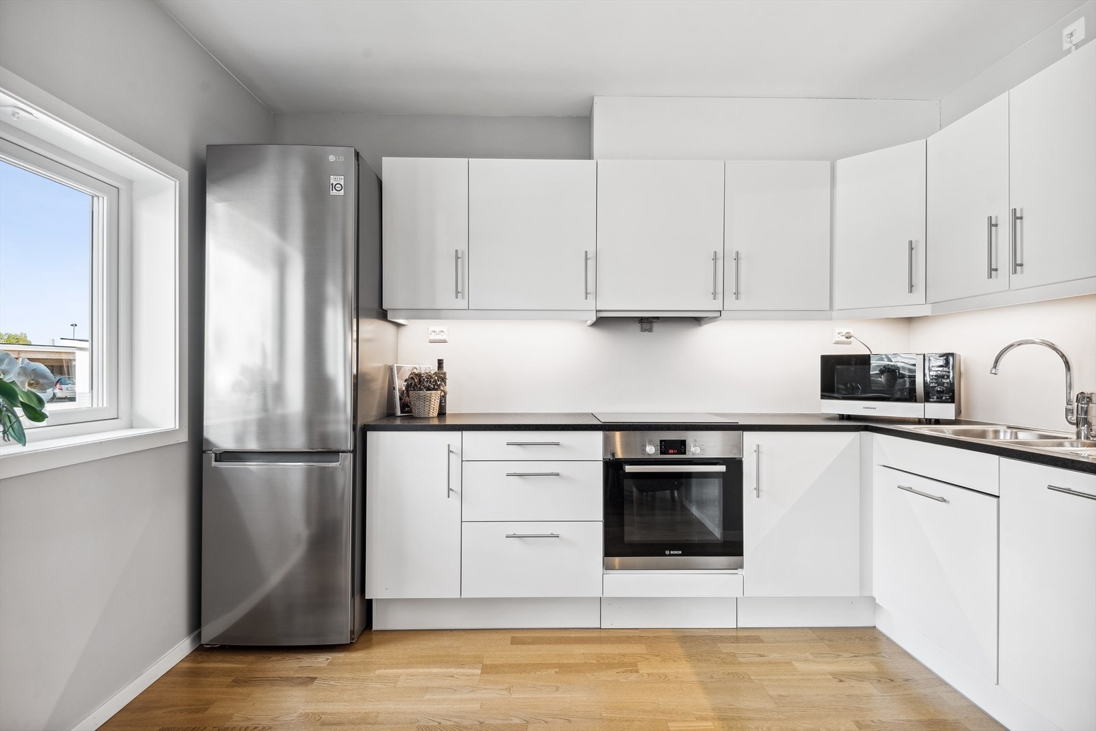 Delikat hvit kjøkkeninnredning fra HTH, med glatte fronter og laminat benkeplate. Kjøkkenet har integrert stekeovn, koketopp og oppvaskmaskin samt frittstående kjøl/frys. Galleribilde
