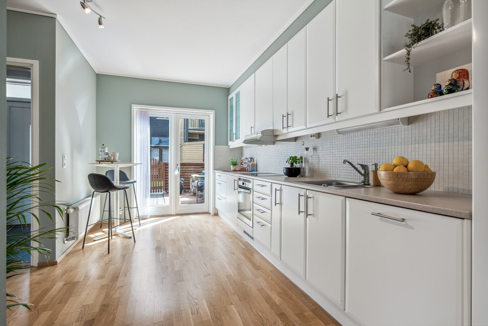 Kjøkkeninnredning med fronter i hvit farge, laminat benkeplate og mosaikkflis på vegg over kjøkkenbenken Galleribilde