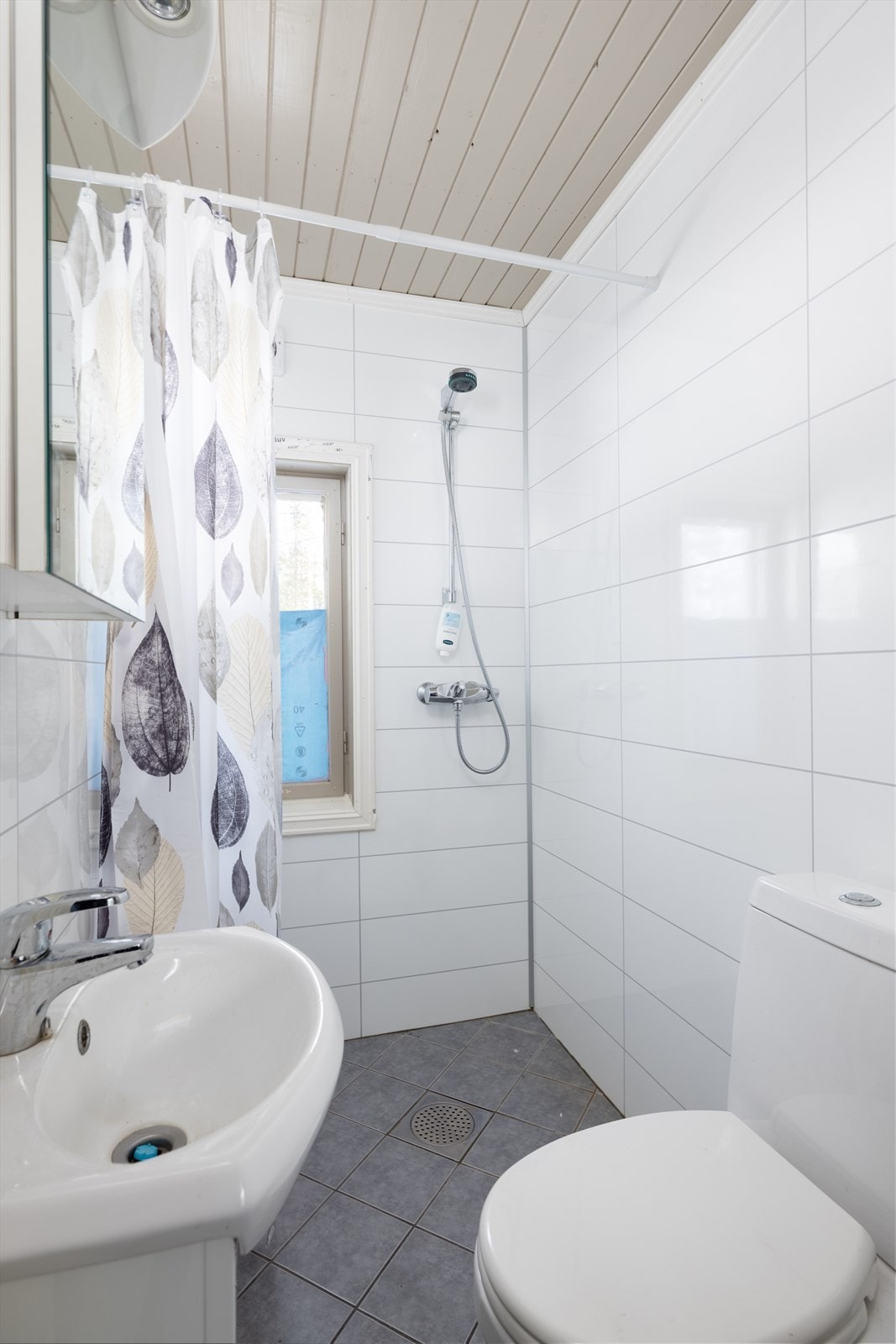 Bad i 1.etasje innredet med servant på innredning, toalett og dusj med forheng. Galleribilde