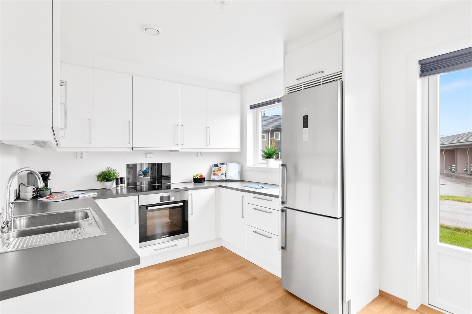 Kjøkkeninnredningen er montert i U-form og har hvite, glatte fronter og grå laminatbenkeplater. Galleribilde