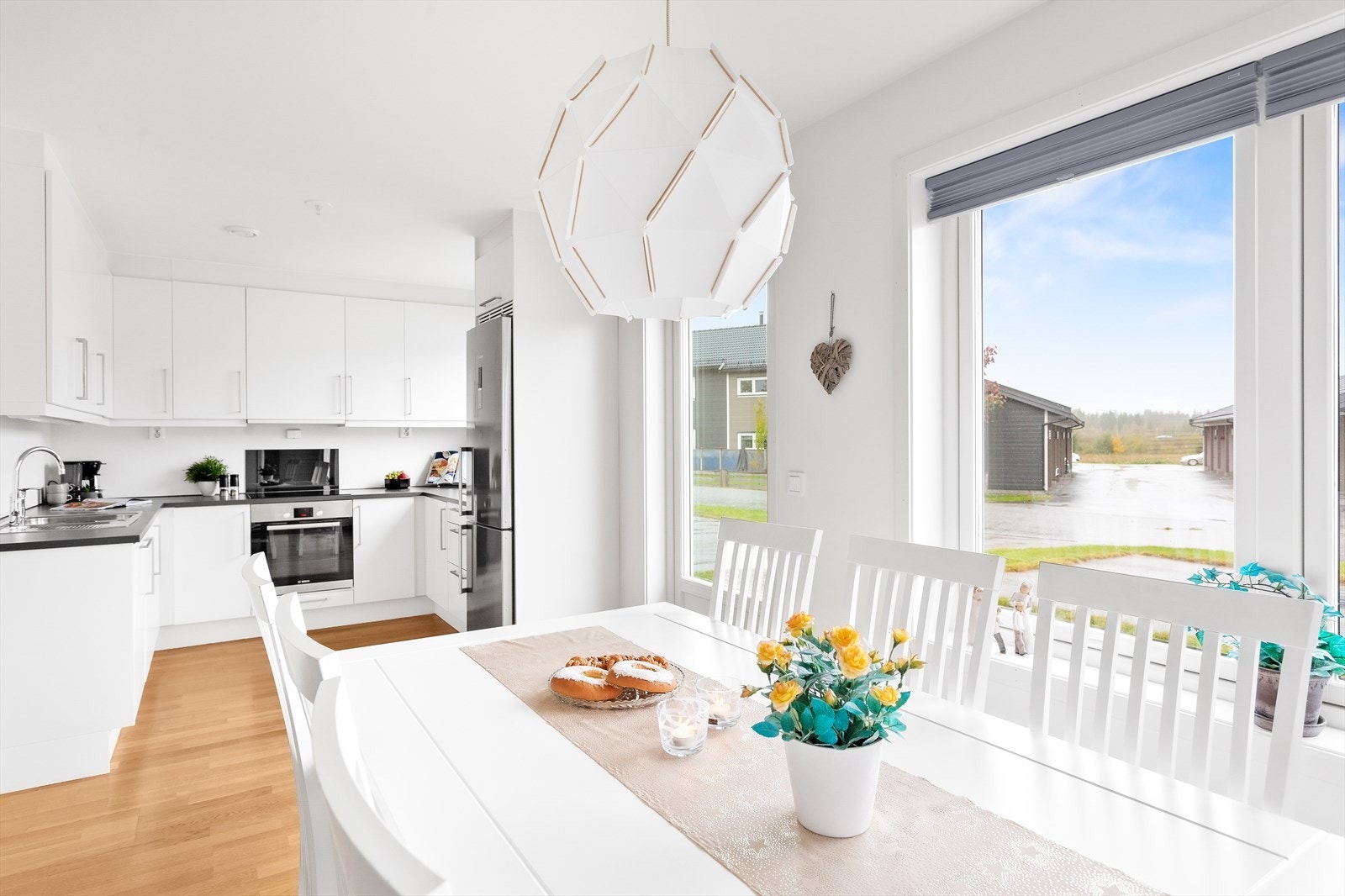 Rommet har flere vinduer med plissegardiner og en verandadør til plenen på inngangssiden. Galleribilde