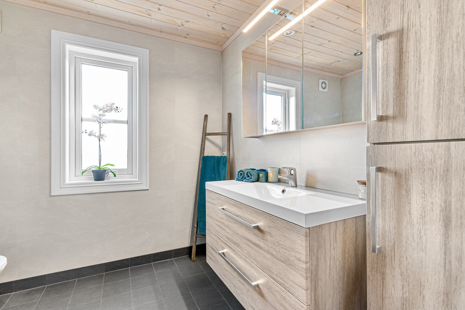 Badet er opplyst å være fra byggeår. Rommet har innredning med nedfelt servant, toalett, dusjkabinett, og opplegg for vaskemaskin og tørketrommel. Galleribilde