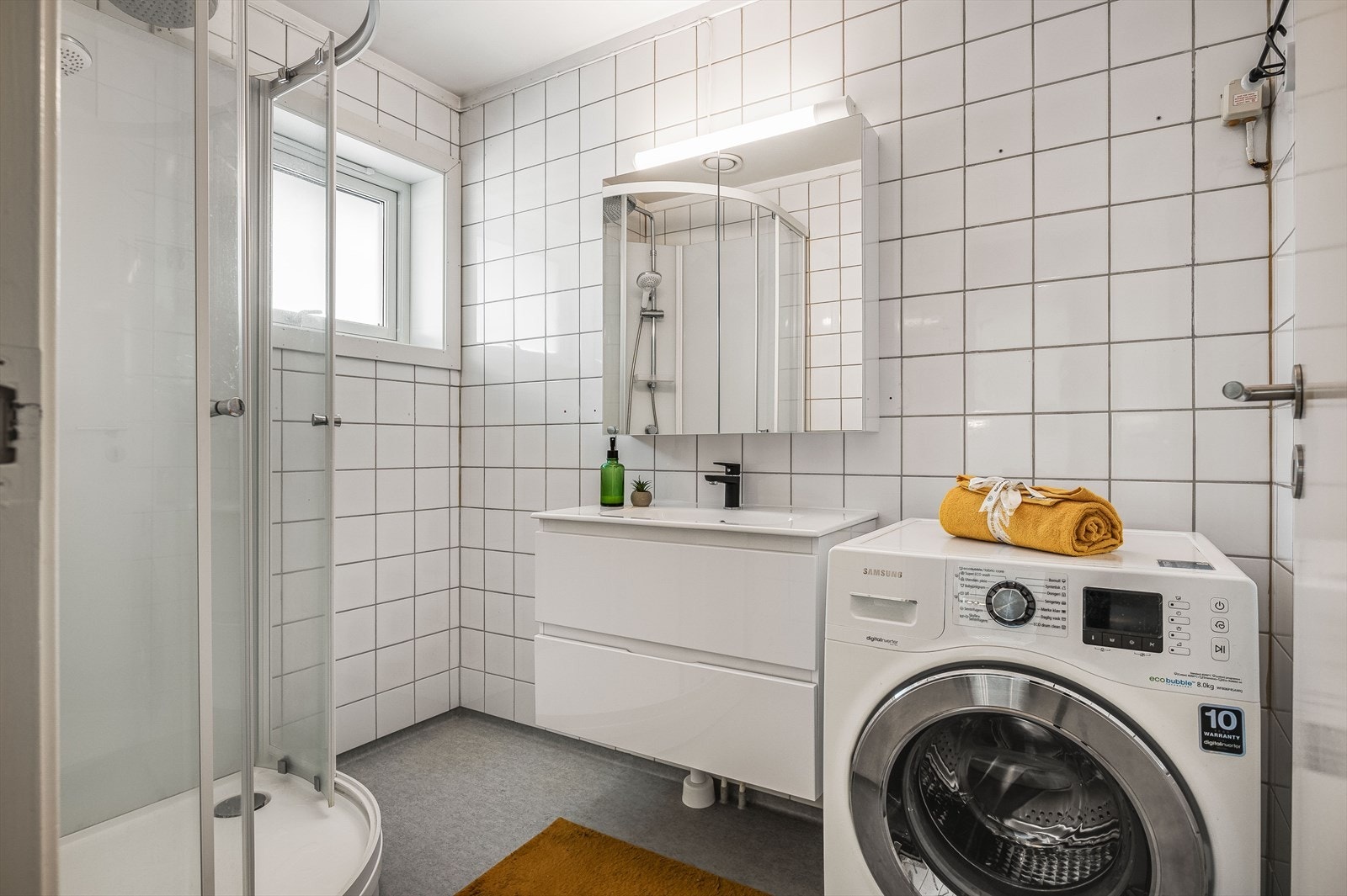 Bad/vaskerom med våtromsbelegg på gulv og flislagte vegger. Rommet varmes opp med panelovn. Galleribilde