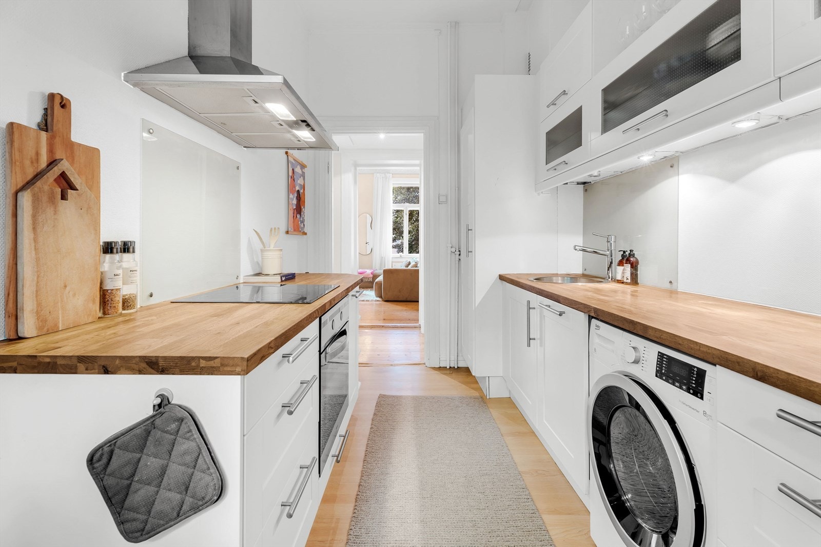 Kjøkkeninnredning med profilerte fronter og heltre benkeplate. Kjøkkenet er utstyrt med platetopp, vaskekum, ventilator, kjøl/fryseskap, ovn, vaskemaskin og oppvaskmaskin. Galleribilde