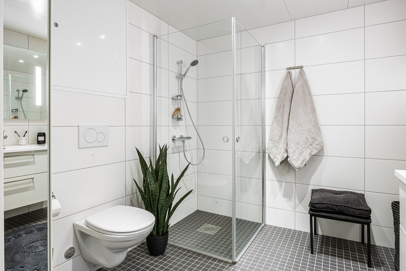 Moderne og flislagt bad på 6m². Badet er utstyrt med behagelig gulvvarme, vegghengt toalett, dusjhjørne med innfellbare dusjdører og opplegg for vaskemaskin. Galleribilde
