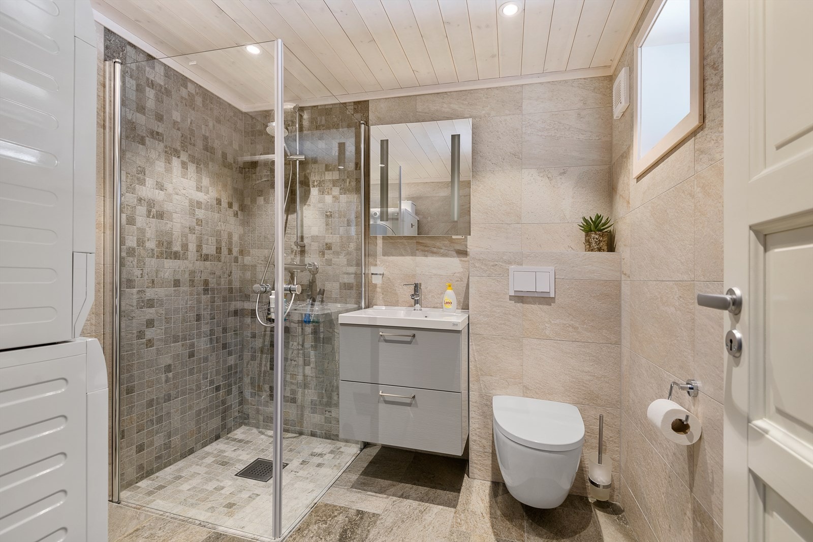 Det ene badet har en lun og innbydende stil. Innredet med dusj, servant og opplegg for vaskemaskin. Galleribilde