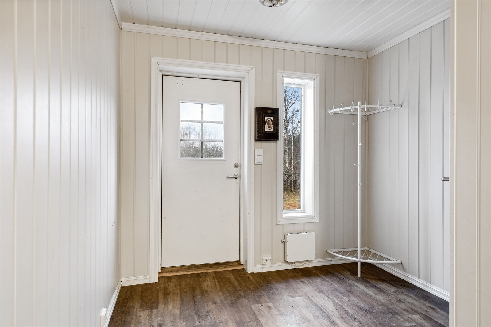 Her kommer man inn i en entré med lysmalte panelplater på veggene og laminat på gulvet. Her er det god plass til å henge fra seg yttertøyet før man vandrer videre inn i boligen. Galleribilde